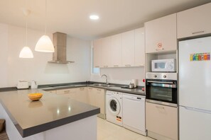 A modern kitchen with white cabinets, a built-in oven, a microwave, a washing machine, and a sink.