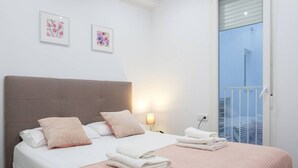 Een slaapkamer met een bed, kussens, een bedlampje, een raam en kunst aan de muur.