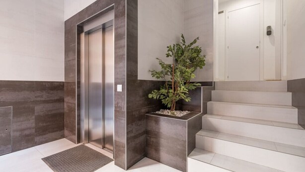 A modern elevator with a metallic finish, a staircase with white steps, and a planter with green foliage. - Spacious Clean & Colourful Apt Quiet Zone (Valencia)