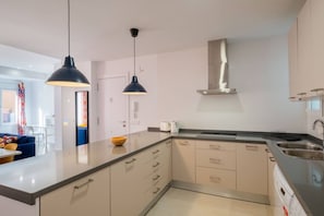 A modern kitchen with a large island, pendant lights, and a stainless steel range hood.