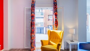 A room with a yellow armchair, a white side table with a lamp, and colorful curtains. - Spacious Clean & Colourful Apt Quiet Zone (Valencia)