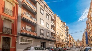 A row of multi-story residential buildings with balconies, parked cars, and a clear blue sky. - Spacious Clean & Colourful Apt Quiet Zone (Valencia)