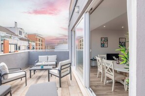 Un balcon avec vue sur les immeubles, un coin repas avec une table et des chaises, et un canapé.