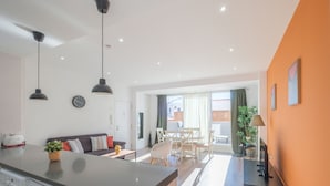 A modern kitchen with a washing machine, a dining area with a table and chairs, and a living space with a sofa and a TV.