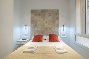 Une chambre d’hôtel avec un grand lit, deux oreillers rouges, une couvre-lit matelassée, deux tables de chevet avec des lampes et un mur à motifs derrière le lit.