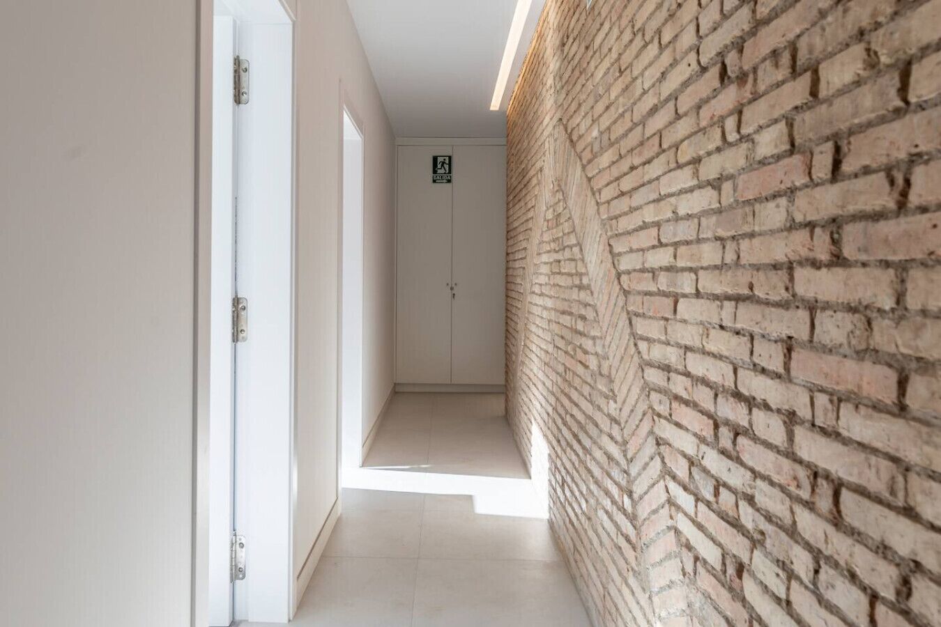Un couloir avec un mur de briques d’un côté et une porte blanche de l’autre.