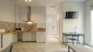 Uma cozinha moderna com micro-ondas, pia e fogão, uma área de jantar com mesa e cadeiras, e uma TV fixada na parede.