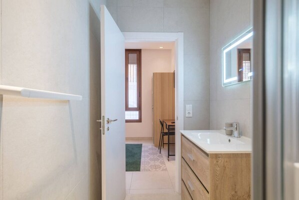 A modern bathroom with a wooden vanity, a large mirror, and a tiled floor.
