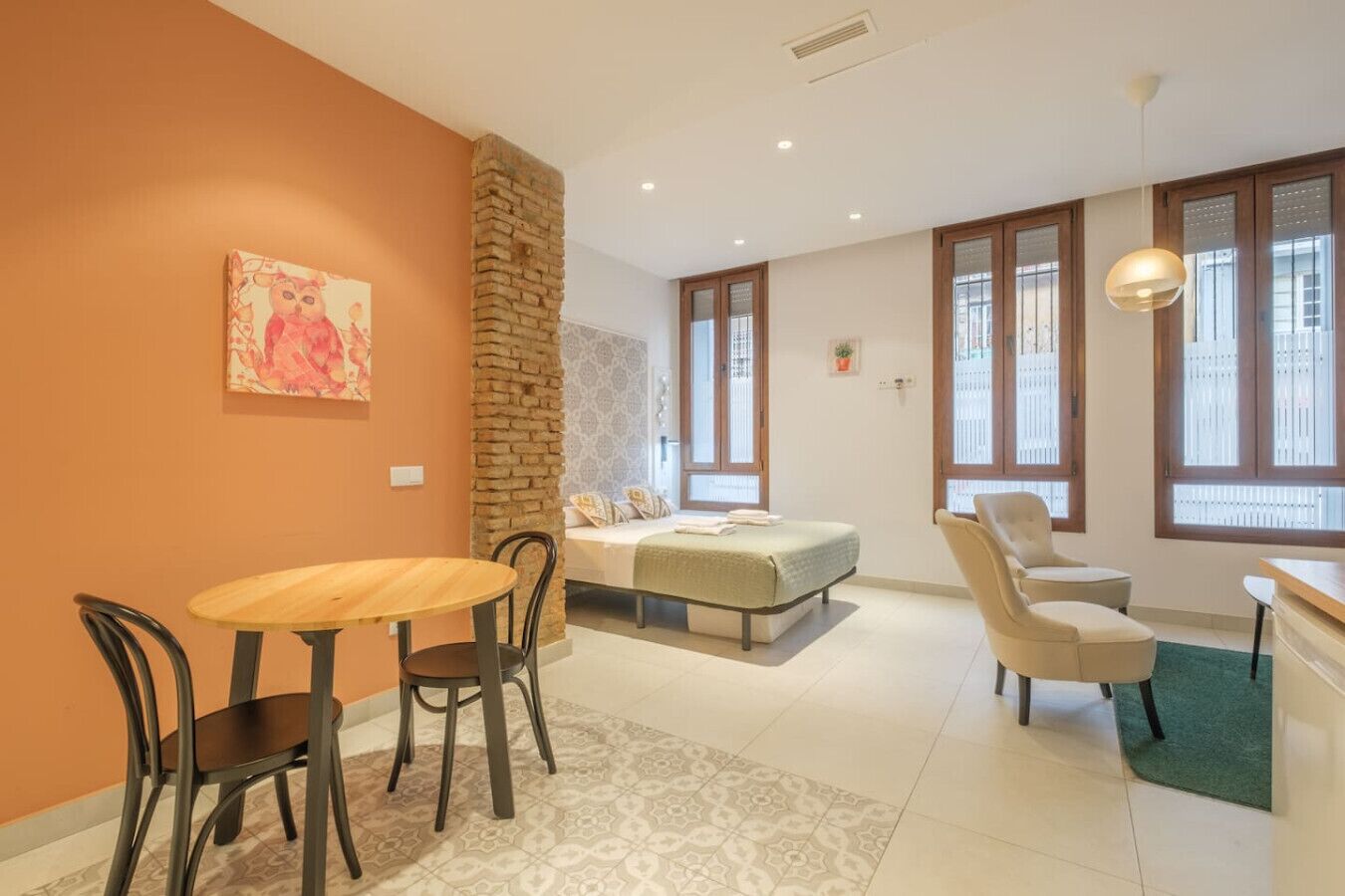 Una habitación acogedora con una cama, una mesa de comedor con sillas, un sofá y un amplio ventanal con persianas.
