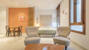 Une chambre à coucher moderne avec un lit, deux fauteuils, une table à manger et une petite table basse.