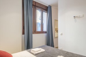 Une chambre à coucher avec un lit, une fenêtre avec des rideaux, une table de chevet et un miroir au mur.