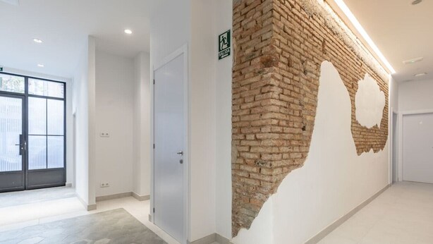 A hallway with a brick wall, a door, and a sign indicating an exit. - Marvellous Apt. with a Large Private Terrace (Valencia)