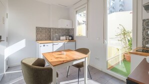 A compact kitchen with a wooden table and two chairs, a window with a view of buildings, and a balcony with a potted plant. - Marvellous Apt. with a Large Private Terrace (Valencia)