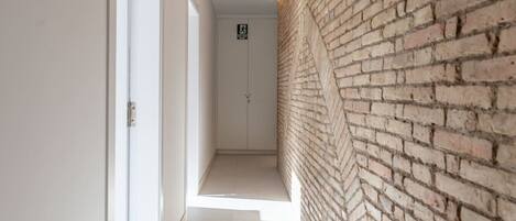 A narrow hallway with a brick wall on one side and white doors on the other.