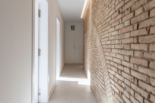 A narrow hallway with a brick wall on one side and white doors on the other.