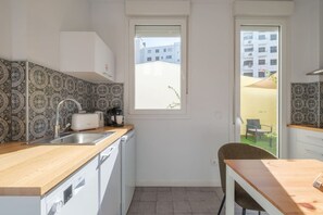 A compact kitchen with a sink, a toaster, and a coffee maker. There is a window providing natural light and a view of buildings outside.