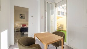 Een moderne kamer met een houten tafel en twee stoelen, een bed met een rood kussen en uitzicht op een tuin door een schuifdeur.