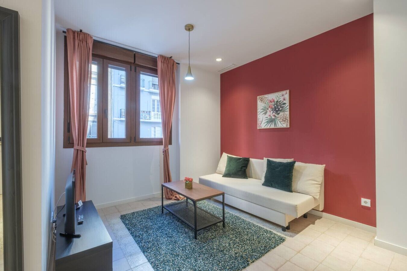 A compact living space with a sofa, a small table, a TV, and a window with curtains.