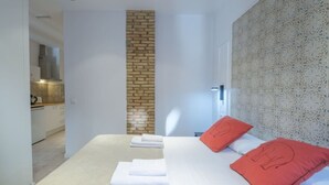 Une chambre d’hôtel moderne avec un mur d’accent en briques, un papier peint à motifs et un lit agrémenté d’oreillers blancs et rouges.