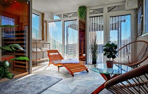 Een ruim balkon met een glazen tafel, rieten stoelen en diverse potplanten.