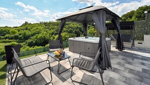 Une terrasse extérieure avec un jacuzzi, un espace salon abrité et une table où sont servis des plats et des boissons.