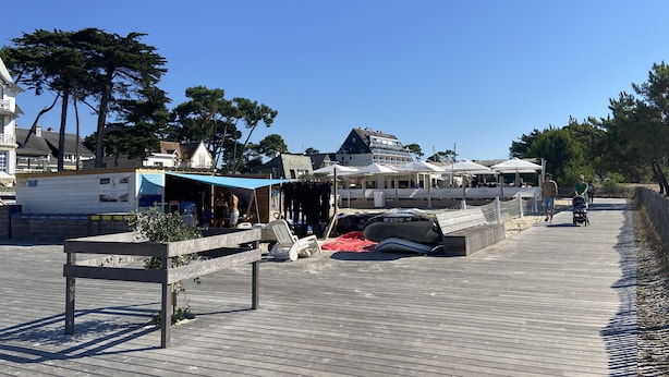 A wooden boardwalk with shops and outdoor seating, a boat, and a signboard. - MILN - Apartment in holiday rental, beach center of Carnac - T11 (Carnac)