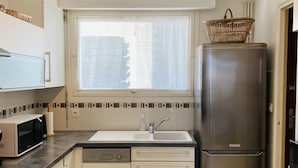 A compact kitchen with a dishwasher, a stainless steel refrigerator, a microwave, and a window with a view of buildings. - MILN - Apartment in holiday rental, beach center of Carnac - T11 (Carnac)