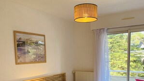 A hotel room with two beds, a window with a view of greenery, a ceiling lamp, and a framed picture on the wall. - MILN - Apartment in holiday rental, beach center of Carnac - T11 (Carnac)