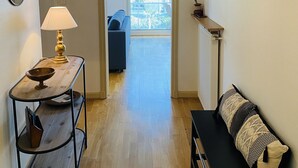A hallway with a wooden floor, a table with a lamp, a bench, a sofa, a framed picture, and a door leading to a balcony. - MILN - Apartment in holiday rental, beach center of Carnac - T11 (Carnac)