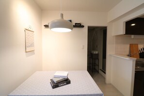 A modern kitchen with a white countertop, a hanging pendant light, and a small shelf with books.