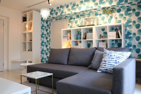 A modern living room with a grey sofa, a small table, and a bookshelf.