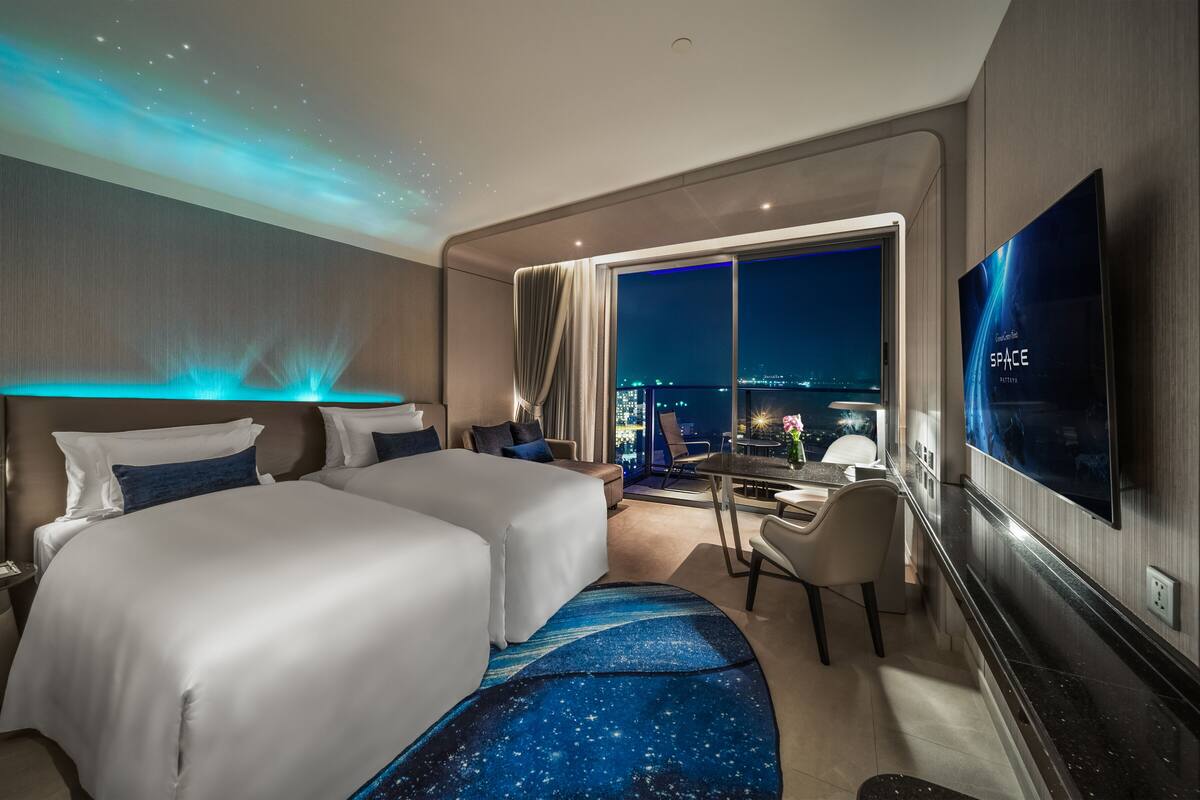 A modern hotel room with two beds, a desk, and a large TV.