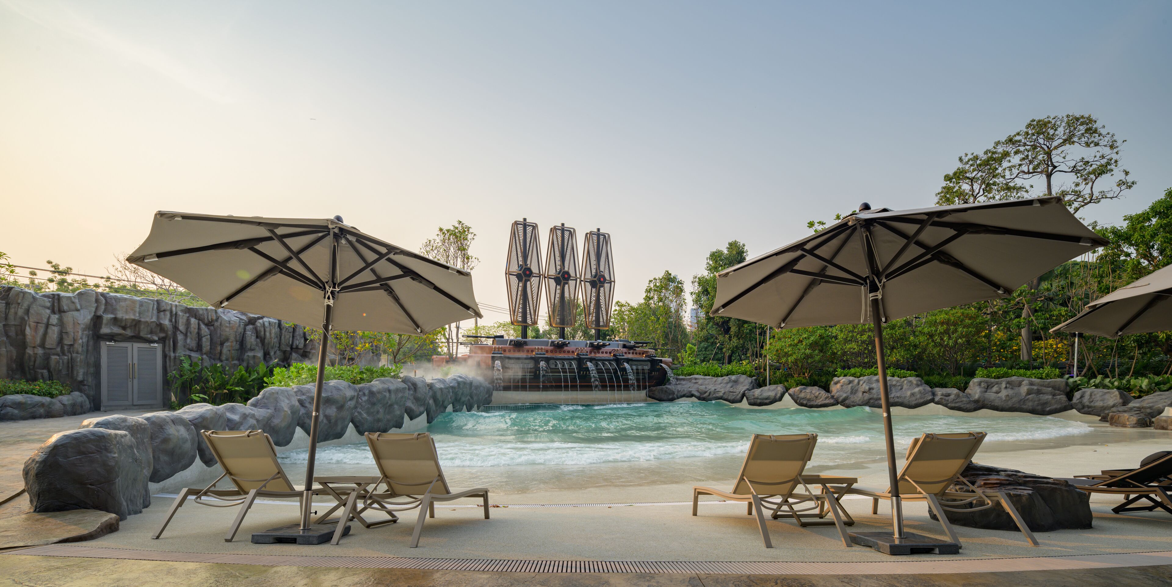 A poolside area with lounge chairs and umbrellas, a waterfall feature, and a rocky landscape.