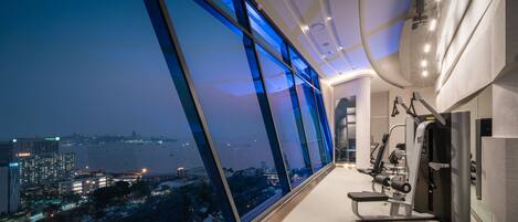 A gym with exercise equipment and a large window offering a city view.