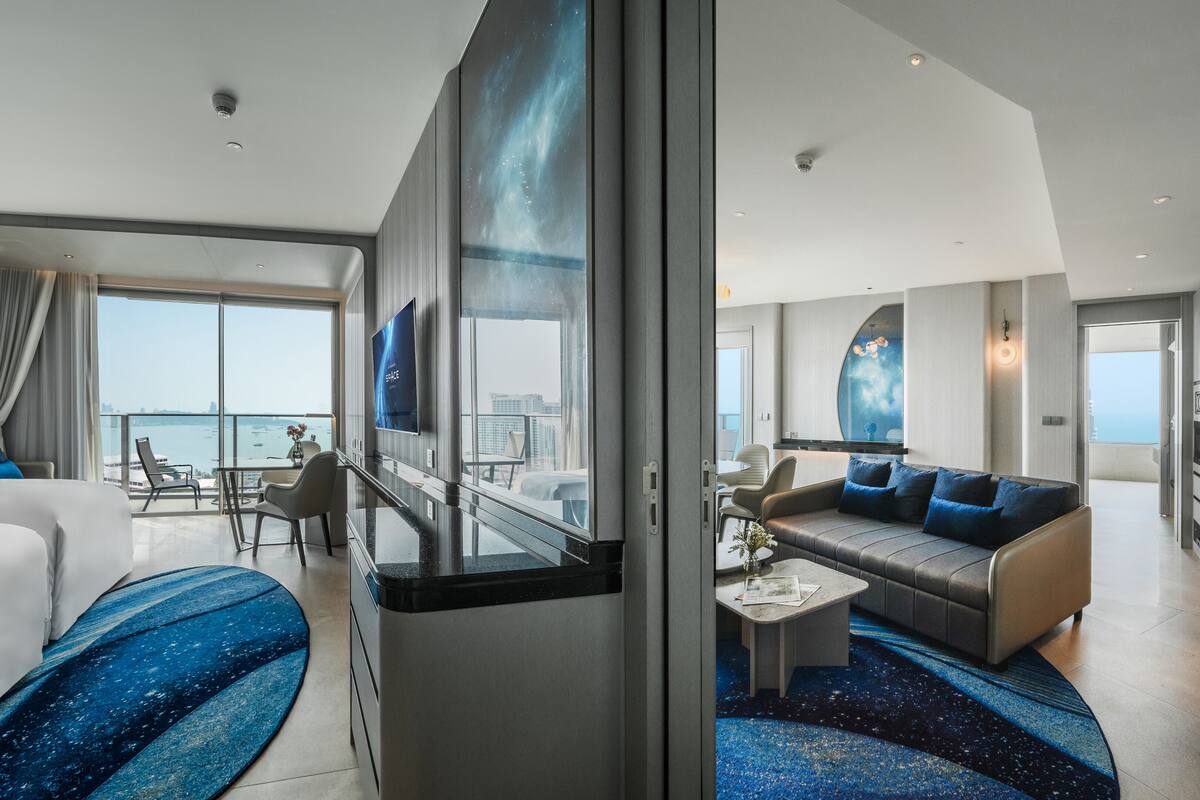 A modern hotel room with a large bed, a sofa, a balcony with a view, and a TV.