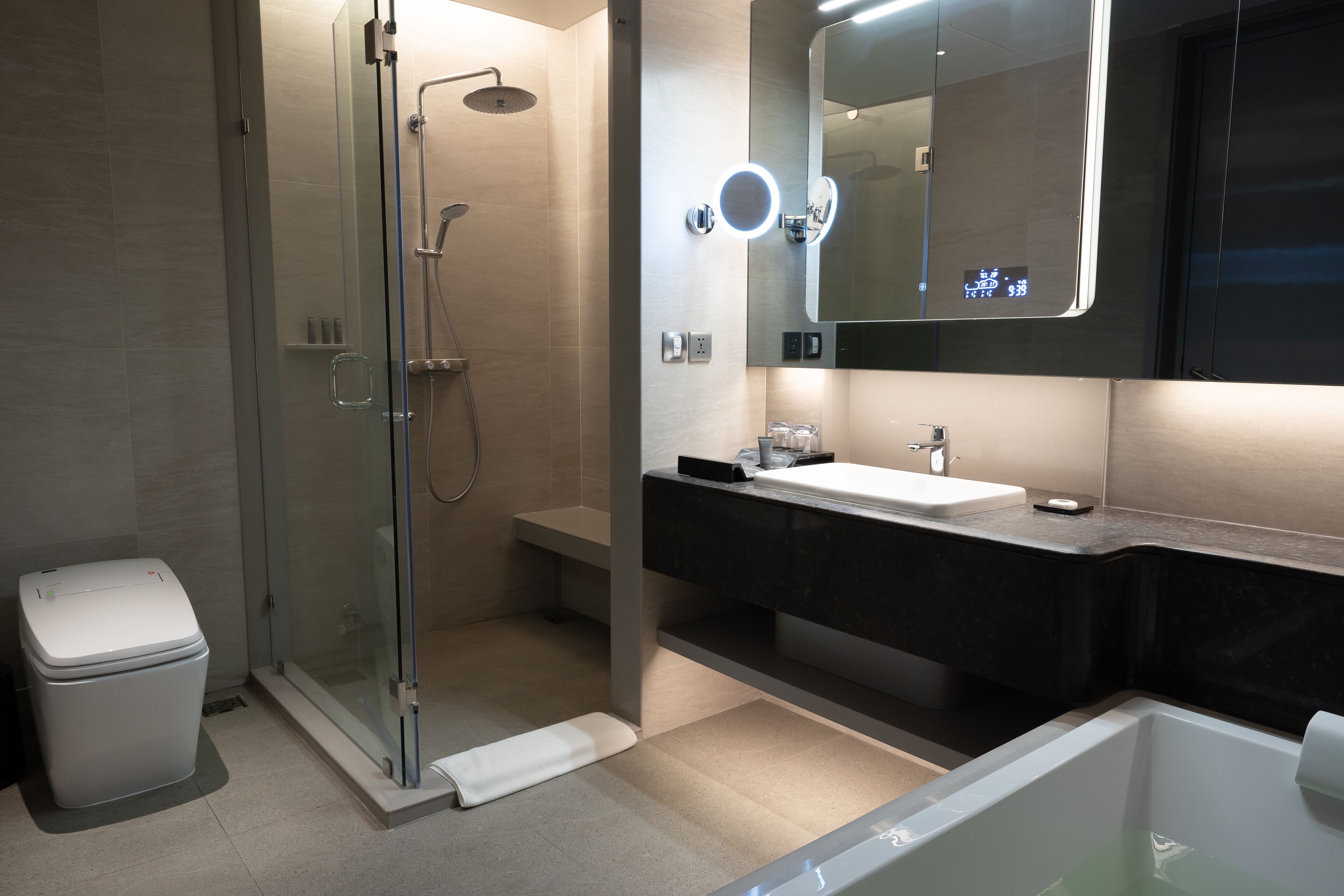 Ein modernes Badezimmer mit einer gläsernen Duschkabine, einem Waschtisch mit dunkler Arbeitsplatte, einem großen Spiegel und einer Badewanne.
