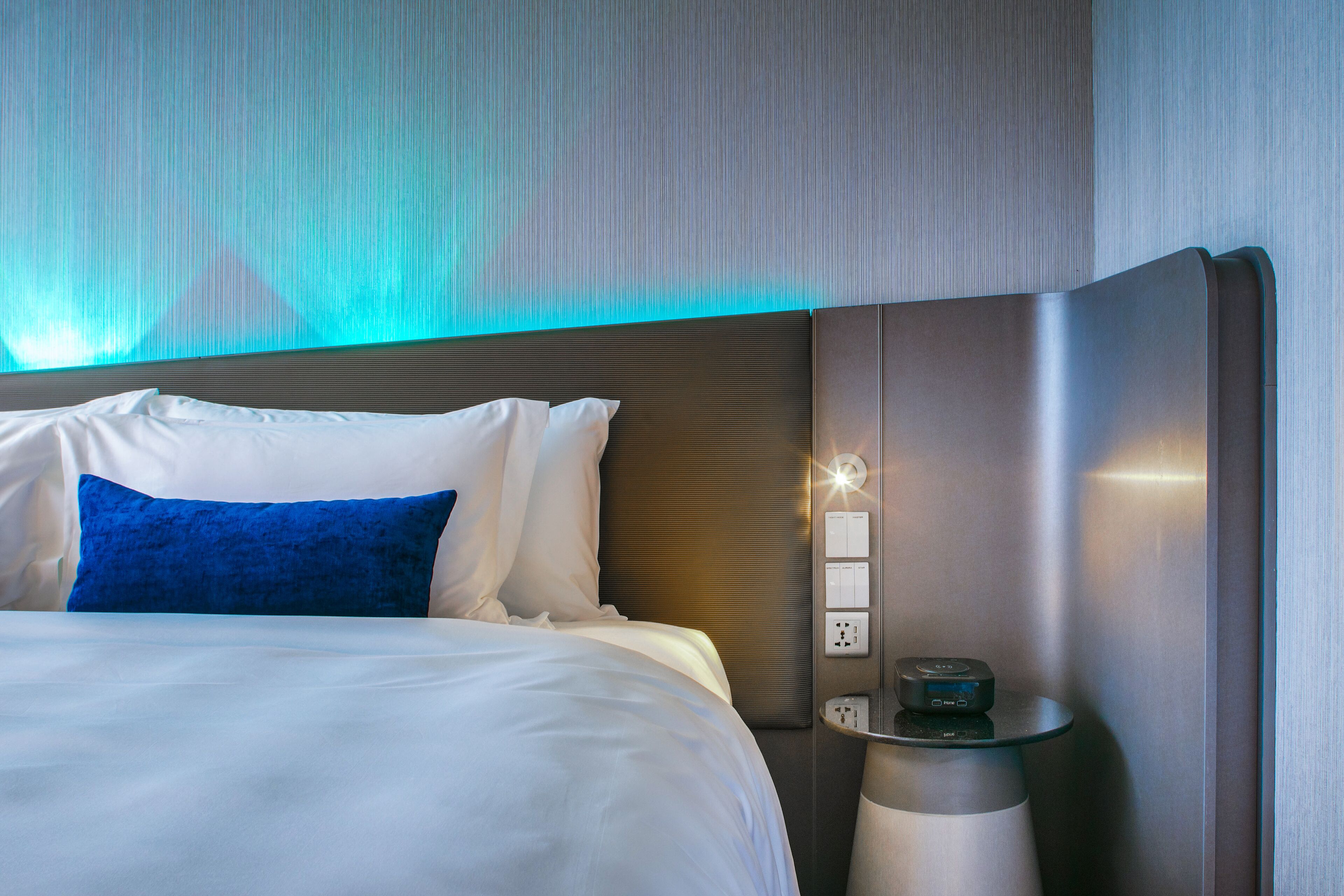 Una habitación de hotel moderna con una cama bien hecha, una mesita de noche con lámpara y un panel de control en la pared.