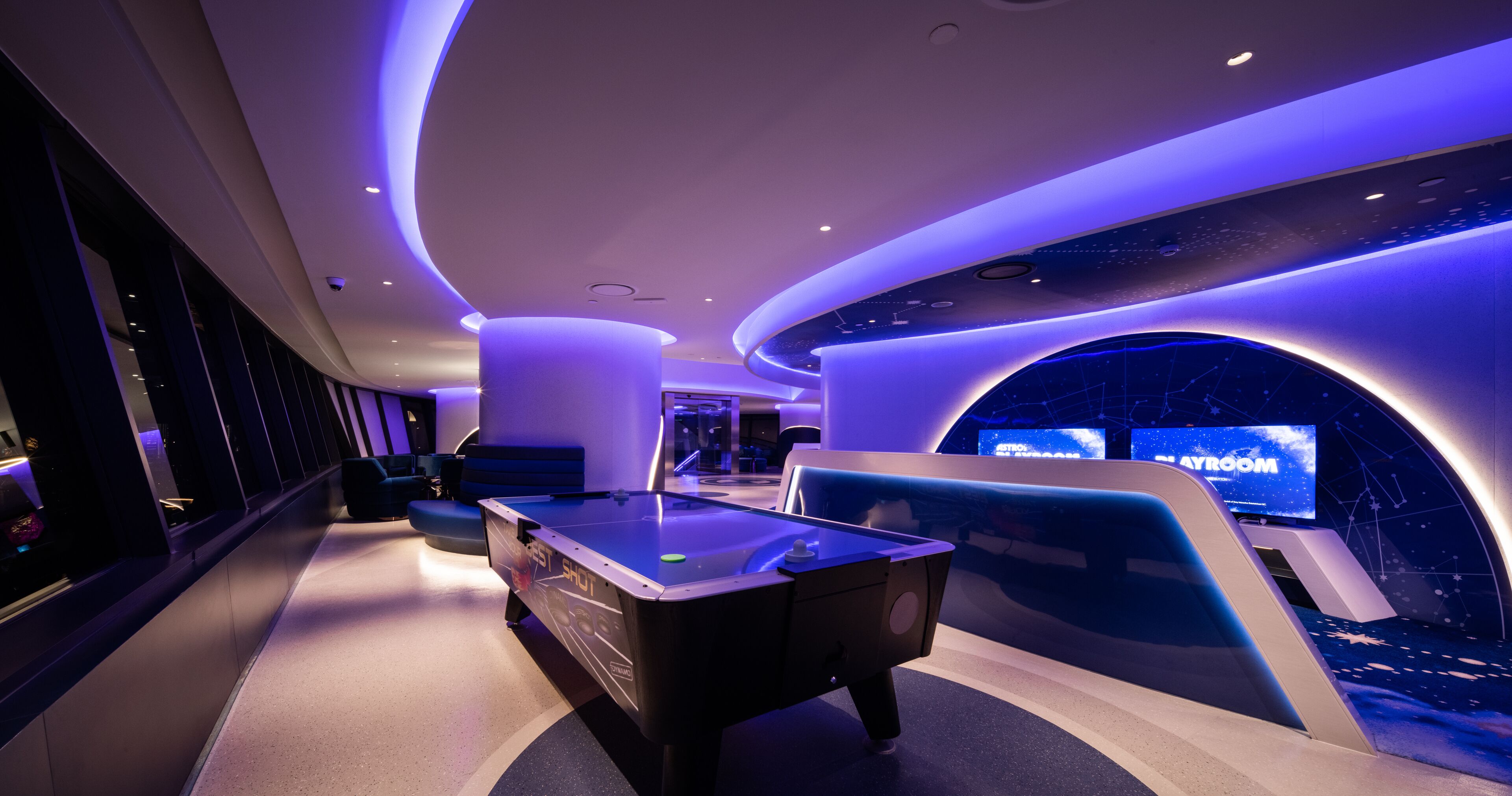 Una mesa de billar moderna con techo iluminado con neón y una pantalla grande que muestra 'STORYROOM'.