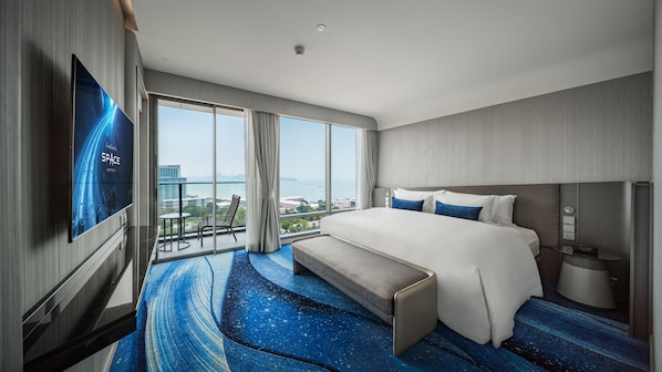 A modern hotel room with a large bed, a TV mounted on the wall, a balcony with a view of the city, and a blue carpet with a space-themed design. - Grande Centre Point Space Pattaya (Pattaya)