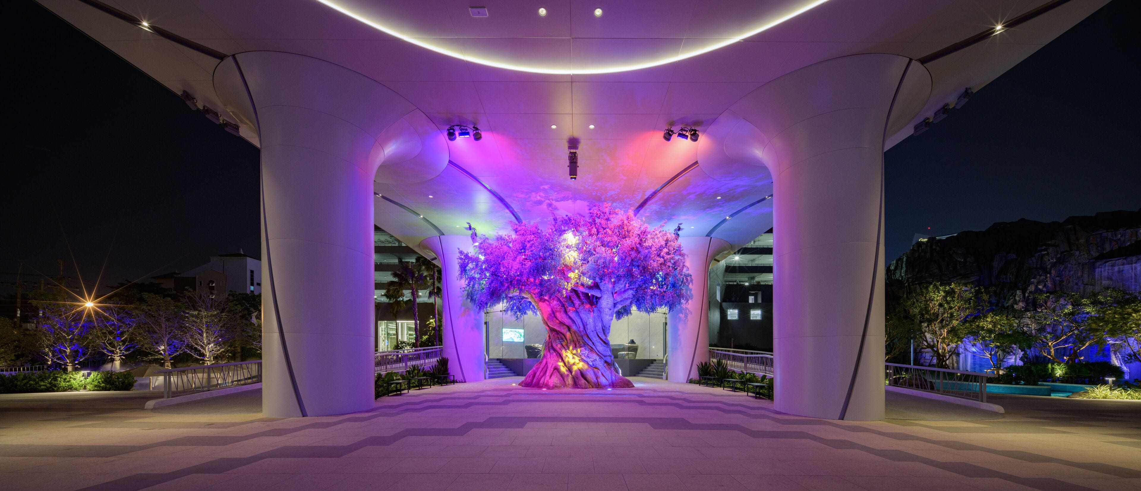 A modern building with a large, illuminated tree sculpture at the center.