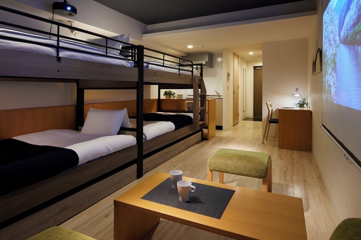 Une chambre avec un lit superposé, un bureau, une chaise et un écran de projection diffusant un paysage.