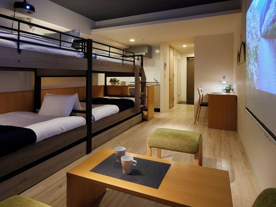 A bunk bed room with a desk, a chair, and a projector screen displaying a landscape.
