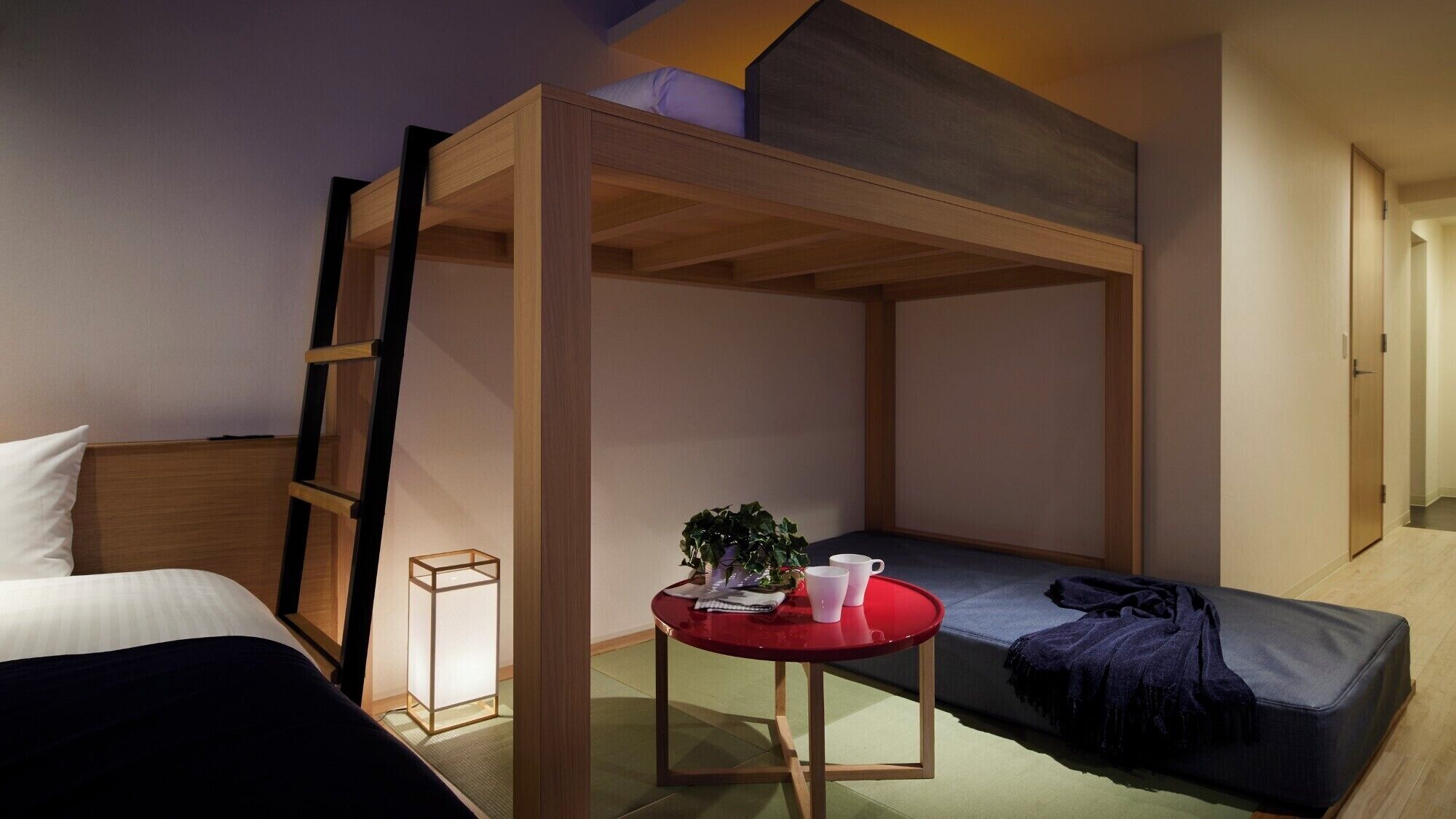 A dorm-style room with bunk beds, a small table with a plant, and a red chair.