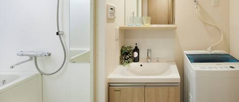 Un baño con bañera, lavamanos, espejo, ducha y lavadora.