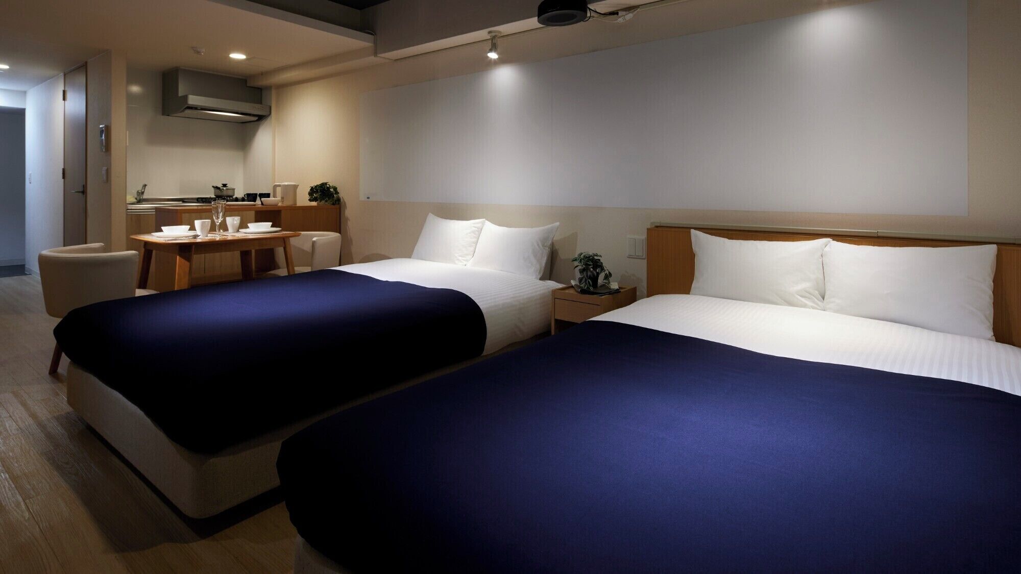 Una habitación de hotel con dos camas, una pequeña mesa de comedor, una silla y una kitchenette.