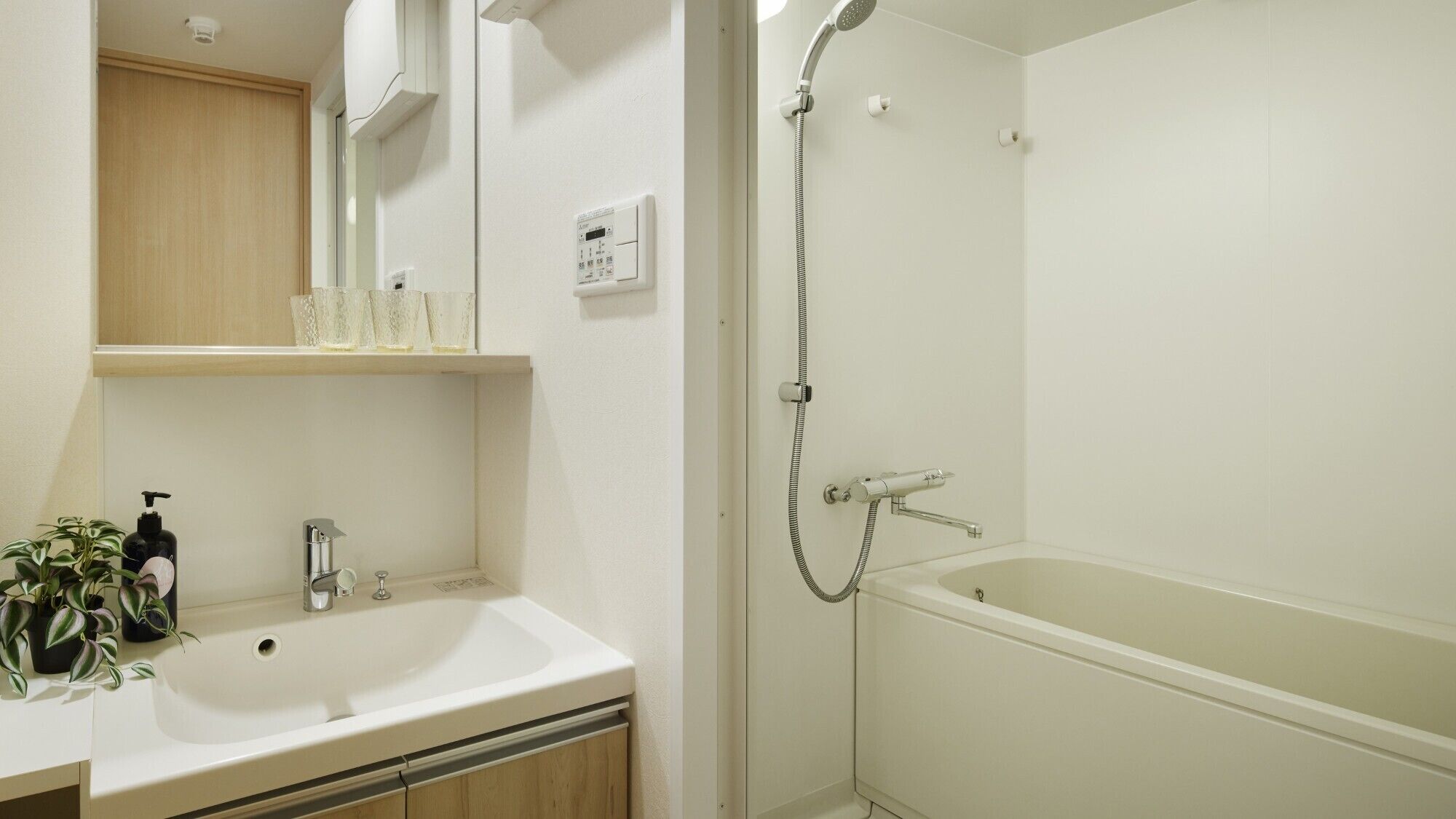 A bathroom with a sink, mirror, shelf with toiletries, and a walk-in shower.
