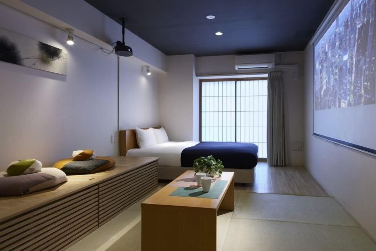 A modern bedroom with a bed, a bedside table, a wall-mounted shelf, and a large window with curtains.