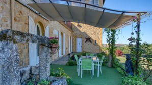 A stone building with a covered patio, green artificial grass, and outdoor furniture. - Magnificent Villa on 50 ha overlooking the medieval town of Domme (Domme)