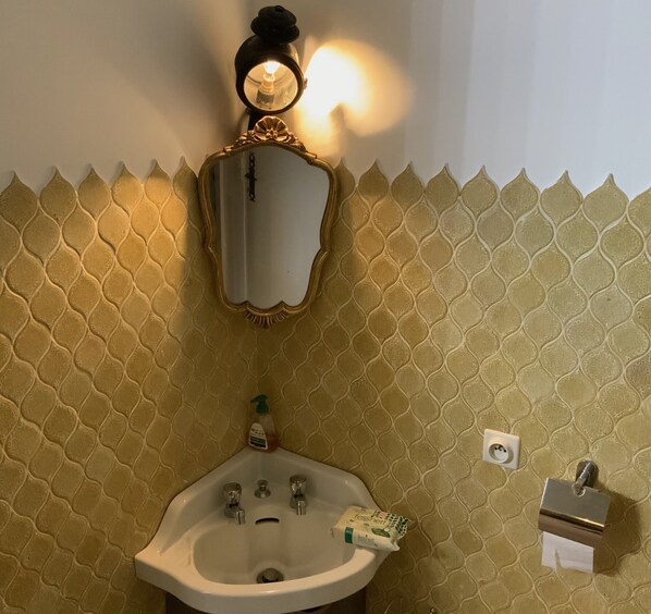 A bathroom with a white sink, a mirror with a gold frame, a soap dispenser, and a towel dispenser.