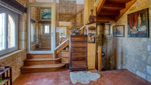 A staircase leading to a second floor with a wooden railing, a large wooden chest of drawers, and a stone wall with artwork. - Magnificent Villa on 50 ha overlooking the medieval town of Domme (Domme)